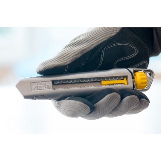 Photo of STANLEY 0-10-018 utility knife with gray and yellow design, held in a gloved hand, side view.