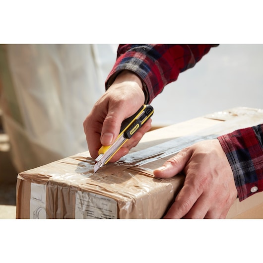 Photo of hands using STANLEY 0-10-475 utility knife to cut open a taped cardboard box.