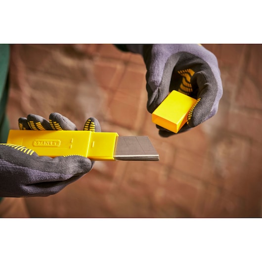 STANLEY 0-11-325 yellow blade dispenser held in gloved hands, showing multiple utility blades.