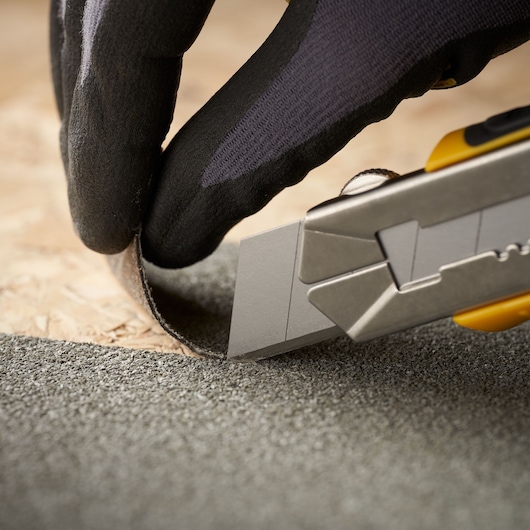 STANLEY 0-11-325 utility knife cutting roofing material, close-up photo shows blade edge and gloved hand.