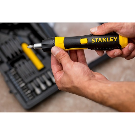 STANLEY 0-63-038 ratcheting screwdriver with black and yellow handle held in hand, tool kit in background.