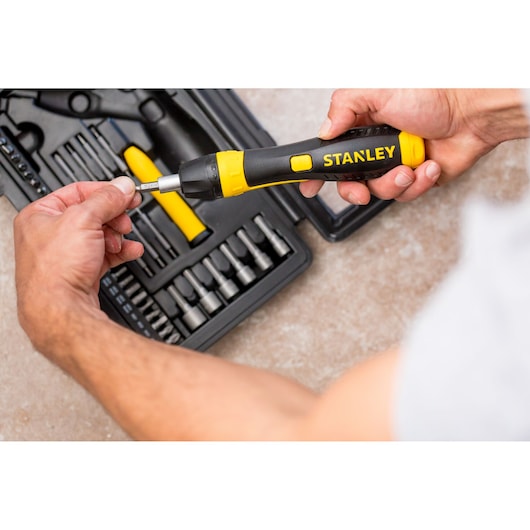 STANLEY 0-63-038 ratcheting screwdriver set with black and yellow handle, person inserting bit, top view.