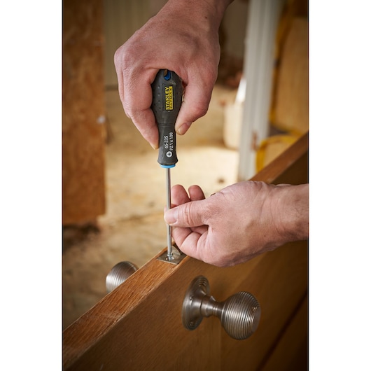 Photo of STANLEY 0-65-335 screwdriver used to tighten screw on metal hinge in wooden door.