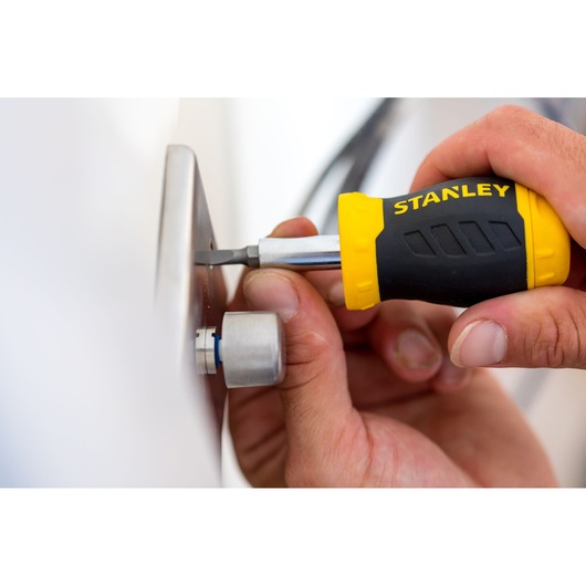 STANLEY 0-66-357 screwdriver with yellow and black handle used to tighten a screw on a metal plate.