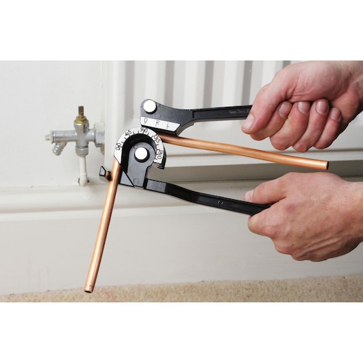 Photo of STANLEY 0-70-451 pipe bender in use, bending a copper pipe near a radiator pipe fitting.