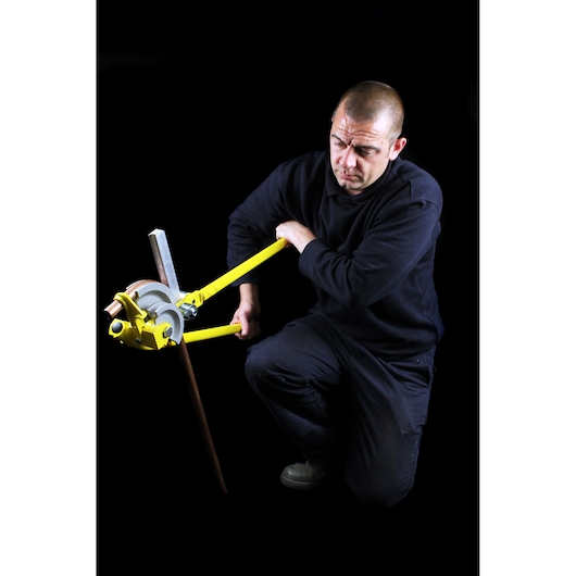 Photo of a person using STANLEY 0-70-452 pipe bender tool on a metal pipe, against a black background.