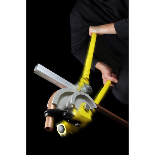 STANLEY 0-70-452 pipe bender with yellow handles shown bending a copper pipe, photographed with user action.
