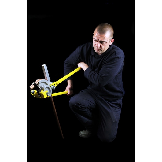 STANLEY 0-70-452 pipe bender in use bending a copper pipe, person kneeling, black background.