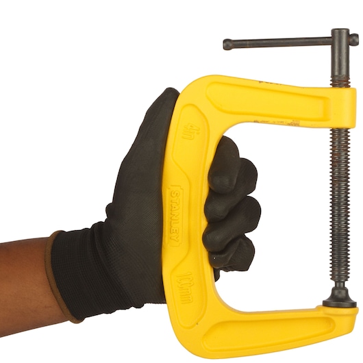Photo of STANLEY 0-83-034 yellow C-clamp held in a gloved hand, clamp facing right, white background.