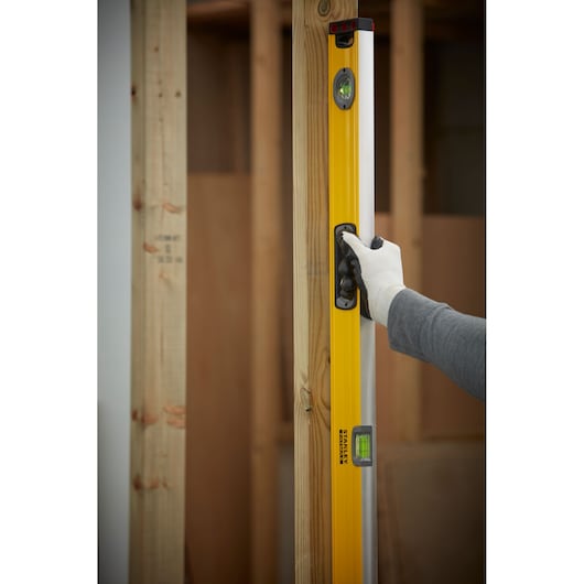 STANLEY 1-43-548 level tool held vertically against wooden frame, user wearing glove.