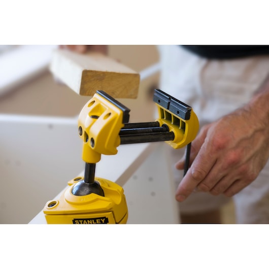 Stanley 1-83-069 adjustable yellow vise clamp holding wood, used in carpentry, close-up photography.