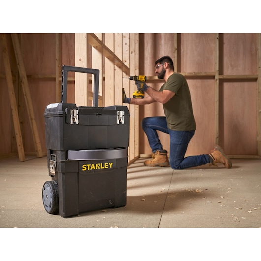 STANLEY 1-93-968 mobile tool chest with wheels in workshop, worker using power tool in background.