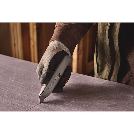 Photo of STANLEY 10-099 utility knife cutting material, gloved hand holding tool in workshop.