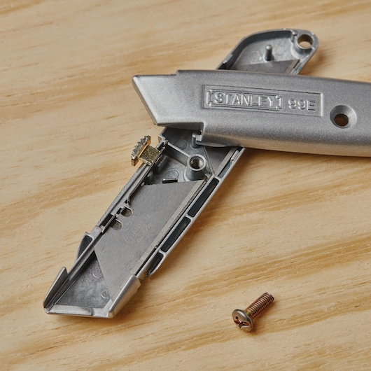 Photo of STANLEY 10-099 utility knife opened with internal parts and screw on wood surface.