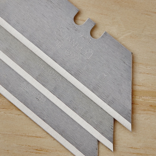 STANLEY 10-099 utility knife blades, close-up of three silver blades with sharp edges on wood surface.