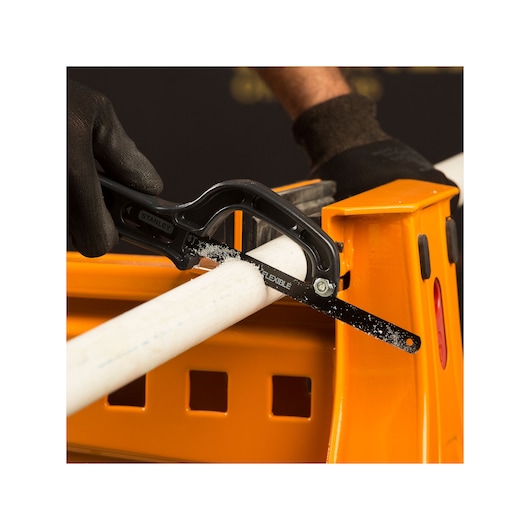 STANLEY 20-807 mini hacksaw cutting white PVC pipe on orange workbench, close-up side angle.