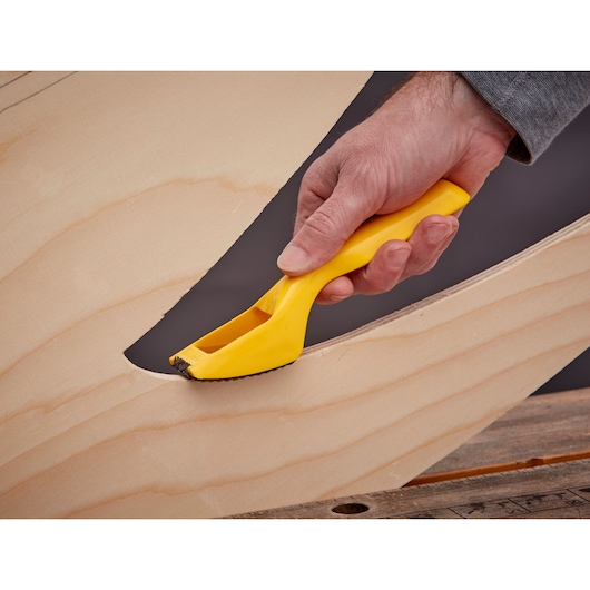 STANLEY 5-21-115 rasp tool with yellow handle smoothing curved wood surface, close-up photo.