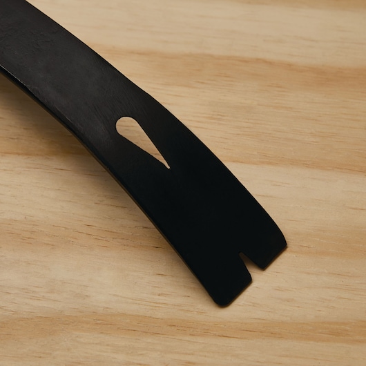 Stanley 55-526 black flat pry bar tip close-up on wood surface, showing nail slot and beveled edge.