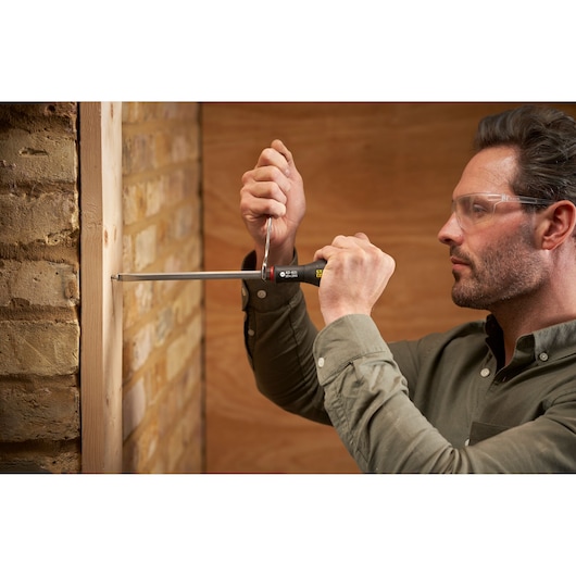 Photo of STANLEY FMHT0-62621 screwdriver used to fasten screw in wooden frame against brick wall.