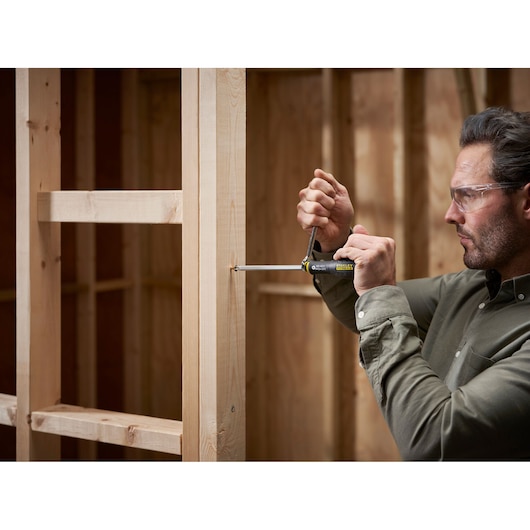 Photo of a person using a STANLEY FMHT0-62623 multi-bit screwdriver on a wooden frame structure, side view.