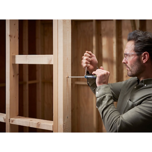 Photo of a person using a STANLEY FMHT0-62624 screwdriver on a wooden frame, construction setting.