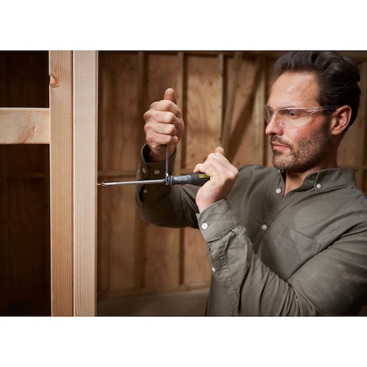 STANLEY FMHT0-62624 screwdriver in use by person attaching screw to wooden frame, close-up action shot.