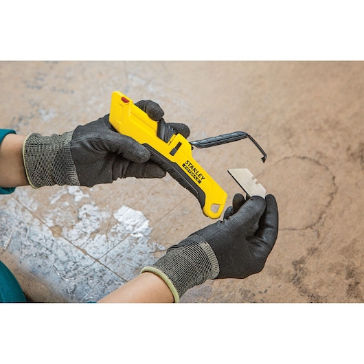 Photo of STANLEY FMHT10365-0 utility knife with yellow handle and blade being replaced by gloved hands.