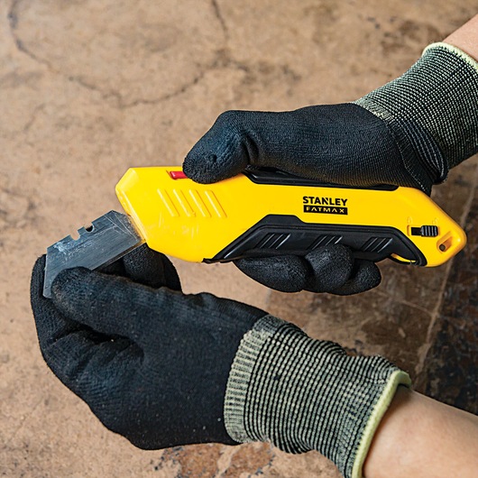 STANLEY FMHT10369 utility knife with yellow and black handle held by gloved hands, showing blade change.