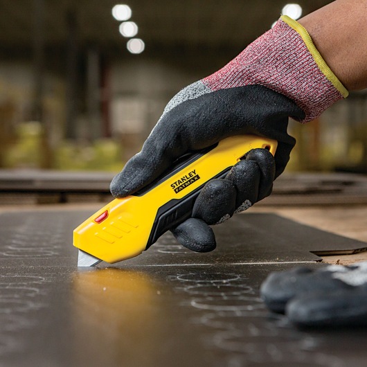 STANLEY FMHT10369 yellow utility knife cutting material, close-up with gloved hand, product photography.