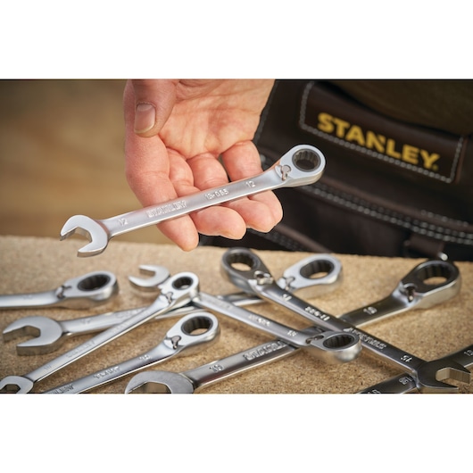 Stanley FMMT13094-0 ratcheting spanner held in hand, with other wrenches on work surface, close-up angle.