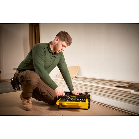 Photo of STANLEY FMMT98107-1 yellow tool box with hand tools, used by a worker kneeling indoors.