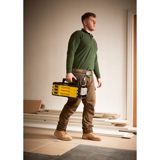 STANLEY FMMT98107-1 tool storage box, yellow and black, carried by worker in construction setting.