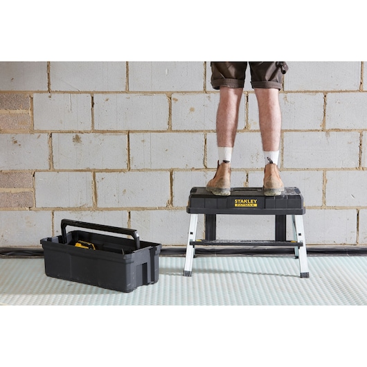 STANLEY FMST81083-1 step stool with man standing, black tool tote on floor, indoor setting.