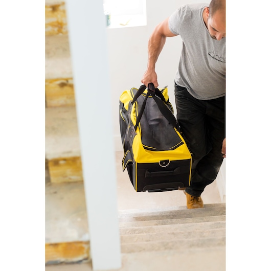 STANLEY FMST82706-1 large yellow and black tool bag carried up stairs, lifestyle context.