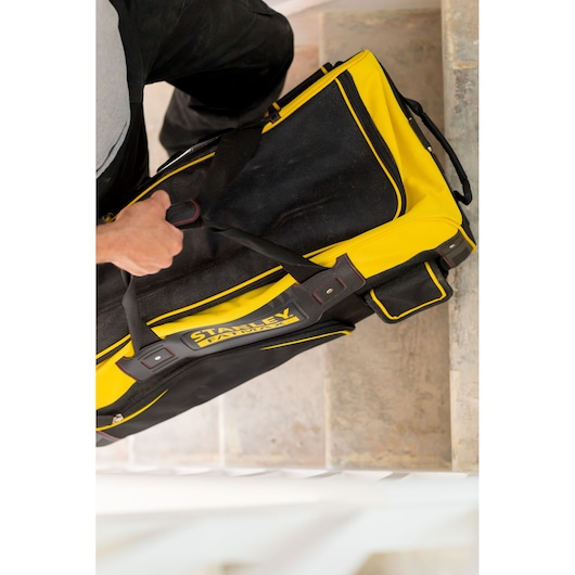 Photo of a STANLEY FMST82706-1 tool bag in black and yellow carried by hand, shown from above on stairs.