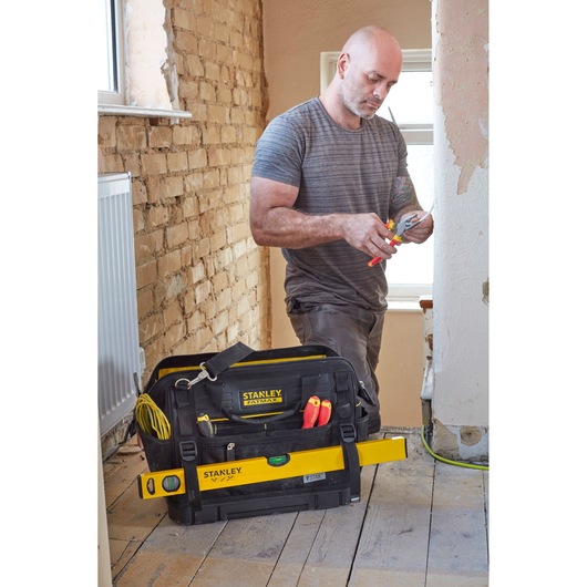 STANLEY FMST83297-1 tool bag on the floor with hand tools and level, worker in the background renovating room.