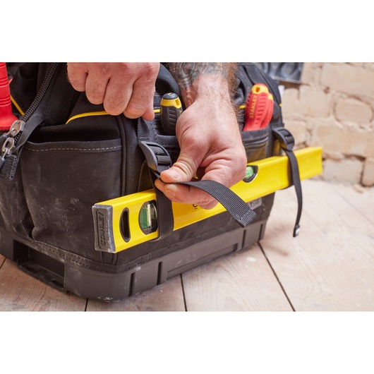 STANLEY FMST83297-1 tool bag held by hand, with yellow level secured on side and tools visible inside.
