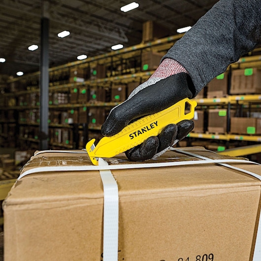 STANLEY STHT10359 yellow safety utility knife cutting box strap, close-up in warehouse.