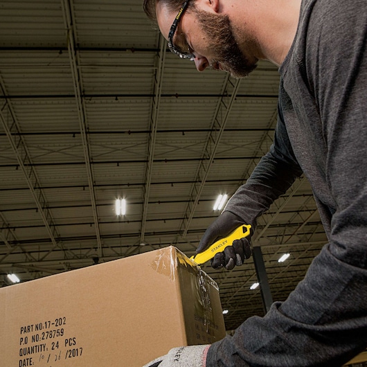 Stanley STHT10359 utility knife cutting box tape in warehouse, visible yellow tool in use.