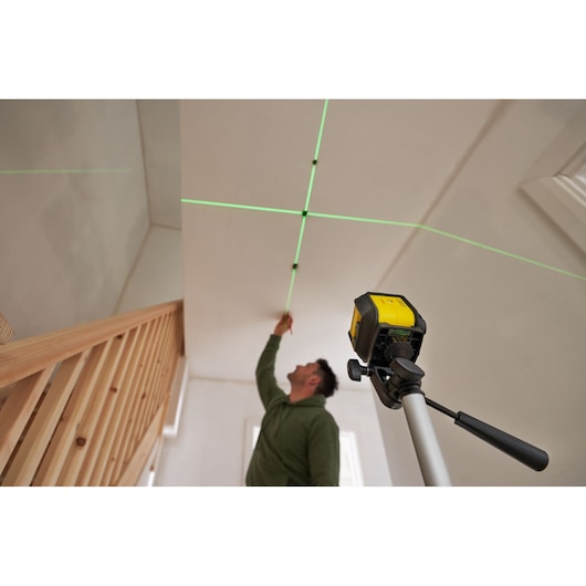 STANLEY STHT77499 laser level projecting green lines on ceiling, mounted on tripod, person marking intersection.