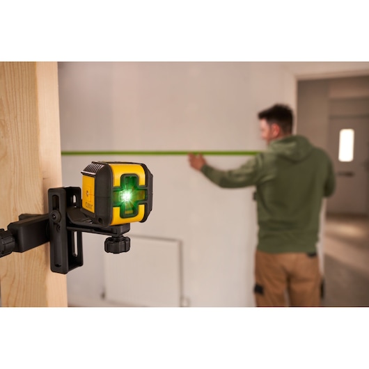 Stanley STHT77499 laser level tool in use, mounted on wood, green laser projecting across a room.