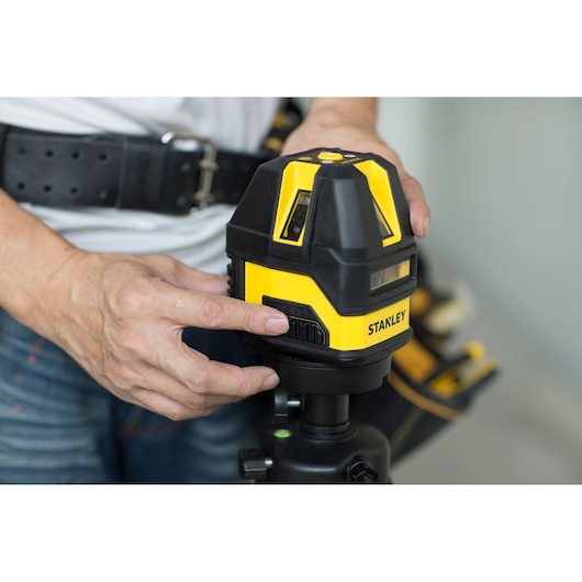 STANLEY STHT77513-8 laser level device held by person, close-up view, yellow and black housing.