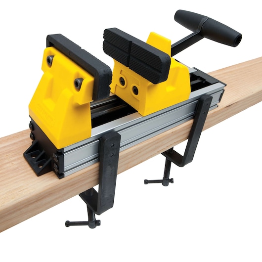STANLEY yellow and black portable bench vise clamped to wood plank, side angle on white background