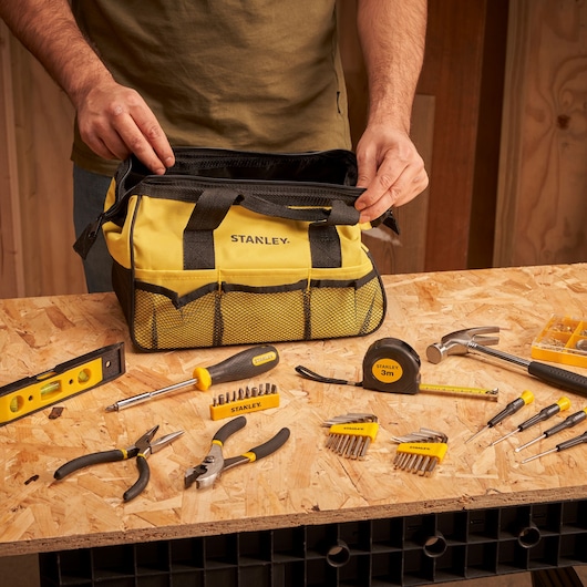 STANLEY STMT0-74101 tool bag in yellow with black accents, surrounded by hand tools on a workbench.