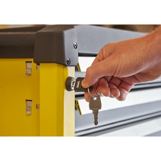 Photo of a hand locking a yellow STANLEY STST74305-1 tool chest with a key, close-up side view.